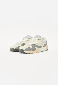 Lacoste sneakers featuring a light cream upper with gray accents, textured overlays, and a thick beige sole with green details.