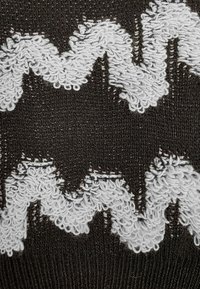 Czarna dzianina z wzorami w zygzak wykonanymi z białej, teksturowanej przędzy, tworząca efekt 3D dzięki kontrastującym kolorom i materiałom.