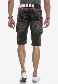 Zwarte denim cargoshorts met rode stiksels, meerdere zakken en een versleten textuur. Gemaakt met een witte gesp met studs en sneakers.