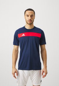 Navy short-sleeve athletic shirt with a red horizontal stripe across the chest, featuring three white stripes and logo detail.