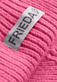Gebreide roze stof met een ribbelstructuur, voorzien van een grijs label waarop "FRIEDA" in donkere tekst is gedrukt.