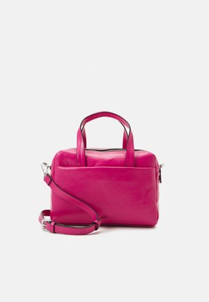 Kleine knallpinkfarbene Lederhandtasche mit oberen Griffen und verstellbarem Schulterriemen auf hellem einfarbigem Hintergrund.