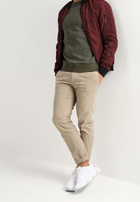 Giacca bomber bordeaux, maglione verde oliva con texture, pantaloni in twill beige e sneakers sportive bianche. Materiali morbidi e design aderente.