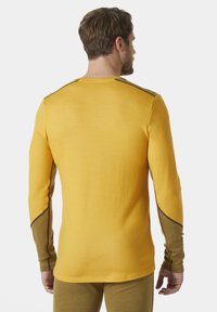 Dlouhá rukávová košile v živé žluté látce se strukturovaným povrchem, s hnědými akcenty na rukávech a ramenou.