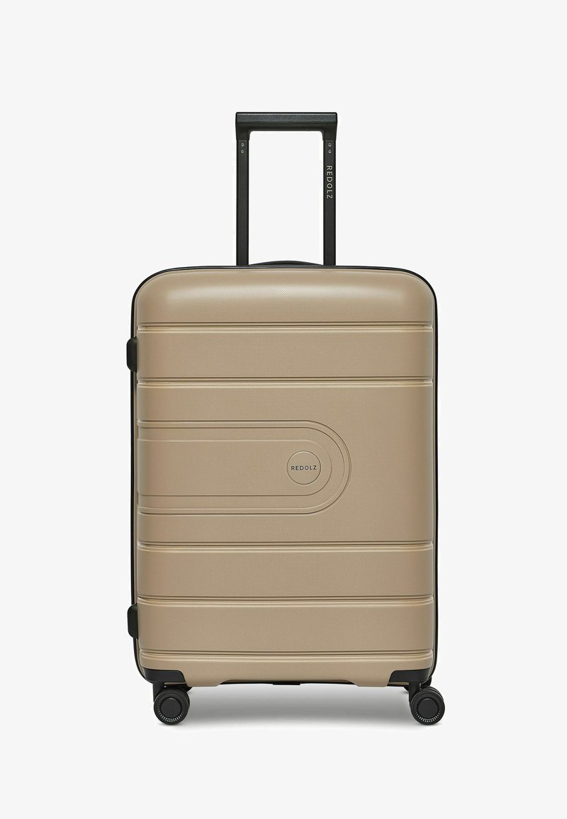 Maleta de concha dura en dorado metálico con acabado texturizado, asa telescópica negra y ruedas, que presenta suaves surcos y un emblema de logo.