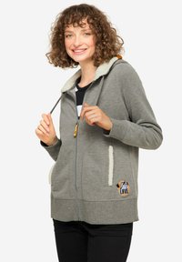 Felpa grigia con cappuccio foderato in bianco e tasche. Presenta un patch "LOVE" nero e arancione. Tessuto morbido con chiusura a zip.