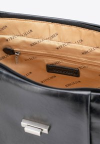 Interno di una borsa in pelle nera con una texture liscia, dotata di una tasca con zip e un'etichetta con logo, foderata in tessuto beige con stampa ripetuta "WITTCHEN".