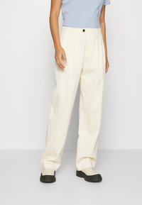 Pantaloni a gamba larga beige chiaro con vita alta, caratterizzati da pieghe frontali e un singolo bottone nero in vita. Tessuto dalla texture liscia.