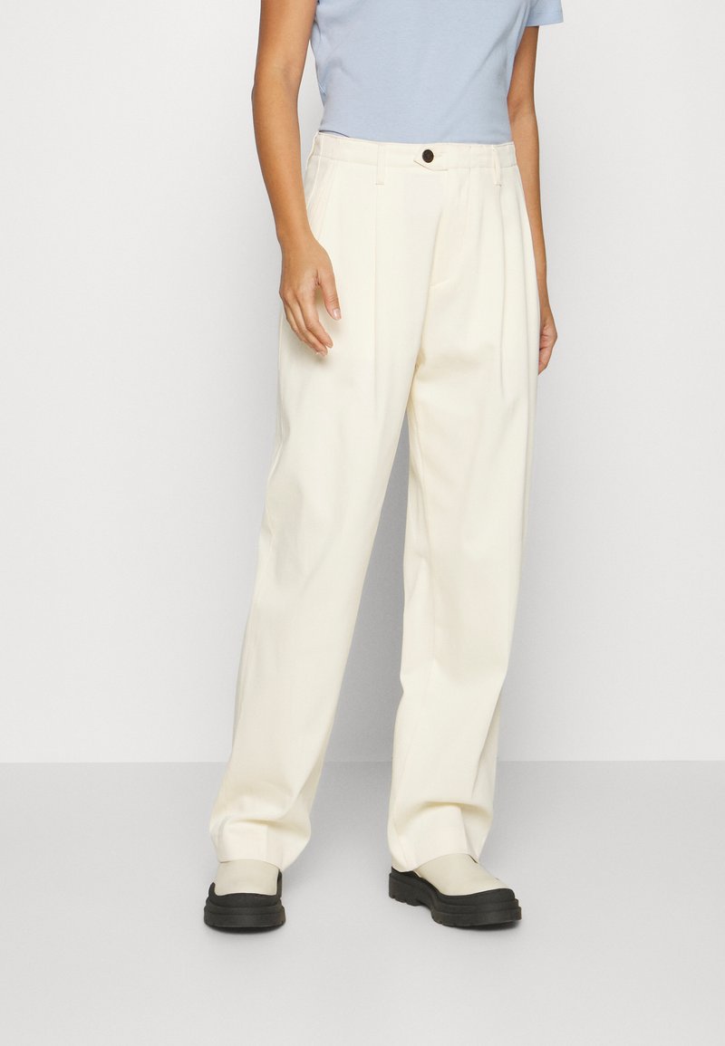 Pantaloni a gamba larga beige chiaro con vita alta, caratterizzati da pieghe frontali e un singolo bottone nero in vita. Tessuto dalla texture liscia.