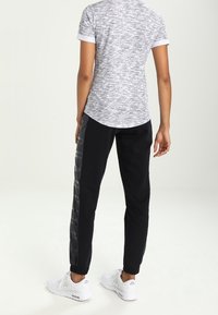 Gray marled short-sleeve shirt, black joggers with glossy side stripes, elastic cuffs, and white sneakers. Positioned from the back.