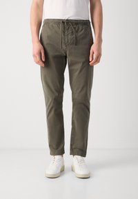 Pantaloni tapered de culoare verde măsliniu, realizați dintr-un material ușor, având un talie elastică cu șnur, buzunare laterale și margini cu manșetă.