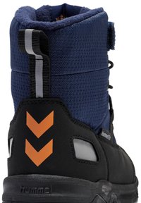 Svart och marinblå stövel med en texturerad ovandel, kontrasterande orange chevron-accenter och en gummisula. Inkluderar en dragrem för enkelt på- och avtagande.