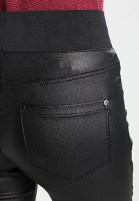 Svarta faux läderbyxor med en elastisk midja, utrustade med en enda bakficka och en slät, glänsande yta.