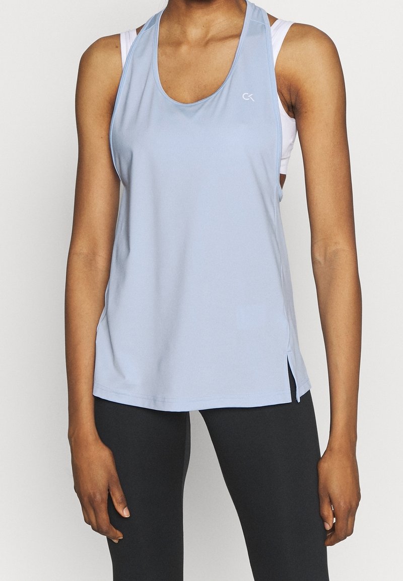 Débardeur de sport bleu clair avec un col rond plongeant, des fentes sur les côtés et un logo sur la poitrine. Confectionné dans un tissu lisse et extensible.