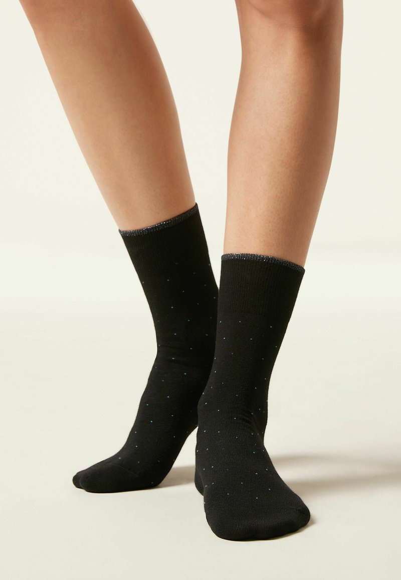 Schwarze Socken mit strukturierter Oberfläche, die kleine blaue Punkte gleichmäßig über den Stoff verteilt aufweisen. Elastische Oberkante für einen angenehmen Sitz.