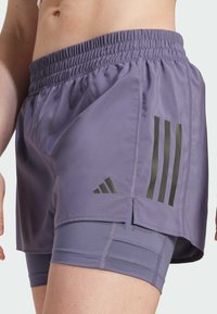 Lila idrottsshorts med elastisk midjeband, innertyg och tre svarta ränder på sidan. Slätt, lättviktigt tyg.