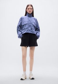 Φωτεινό γαλάζιο κοντό μπουφάν με ψηλό γιακά, δύο μπροστινές τσέπες· συνδυασμένο με μαύρα σορτς και ουδέτερα αθλητικά παπούτσια. Λείο ύφασμα και άνετη εφαρμογή.