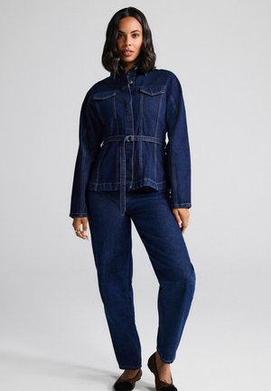 Dunkelblaue Jeansjacke und -hose. Die Jacke besitzt eine taillierte Form mit einem Gürtel und vorderen Taschen mit sichtbaren Nähten. Weicher, strukturierter Stoff.