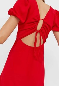 Punainen mekko, jossa on puffihihat, kerätty selkä ja avoin muotoilu, jossa on nauhat. Pehmeä kangas ja sileä tekstuuri parantavat sen yleisilmettä.