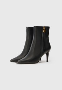 Bottes noires en cuir à hauteur de cheville avec un bout pointu, un talon haut élancé et une fermeture éclair sur le côté, ornées de quincaillerie dorée pour une finition soignée.