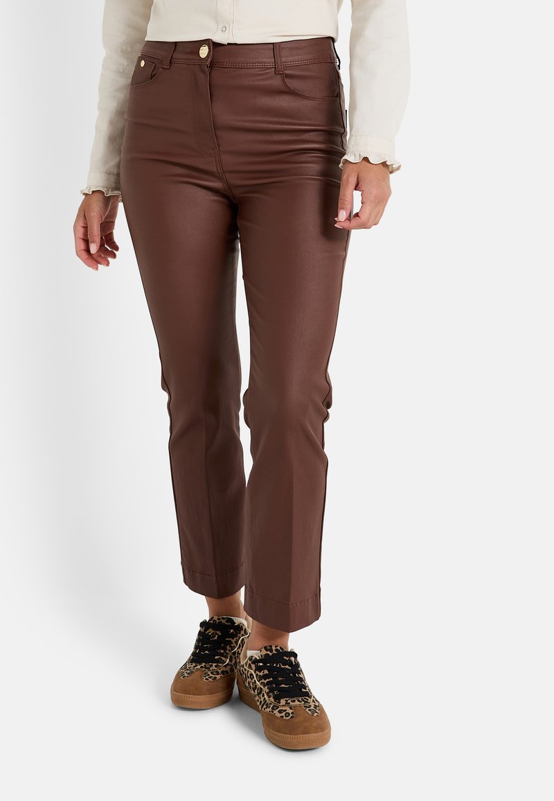 Pantalones de imitación de cuero marrón con un corte ajustado, cintura alta y dobladillo acampanado. Combinados con zapatillas de estampado de leopardo y una camisa de color claro.