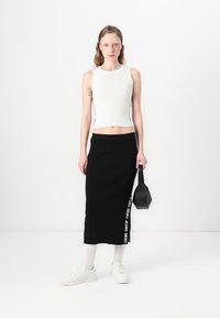Hvit ribbet tanktopp, svart ribbet midi-skjørt med "Dkny Jeans"-tekst, kombinert med hvite joggesko og en liten svart håndveske.