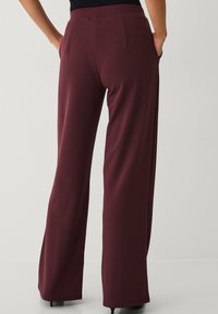 Pantalones anchos color granate con una textura suave, que cuentan con una cintura entallada y bolsillos traseros, creando una silueta estructurada.