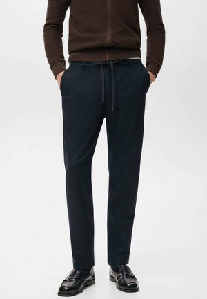 Marinblå byxor med skräddarsydd passform, gjorda av mjukt tyg. Har dragsko och sidofickor. Matchas med svarta läderskor.