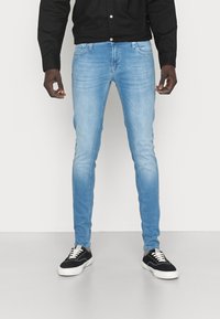 Světle modré slim-fit džínsy se sepraným povrchem, designem s pěti kapsami a mírnými odřeninami, spárované s černobílými nízkými teniskami.