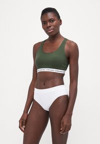 Soutien-gorge de sport en coton vert avec bande logo, associé à une culotte blanche taille haute, mettant en avant un design sans coutures et une texture lisse.
