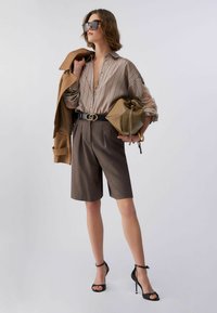 Blouse rayée, short marron sur mesure, ceinture noire avec emblème, lunettes de soleil surdimensionnées, sac beige, sandales à talons hauts, superposition élégante.