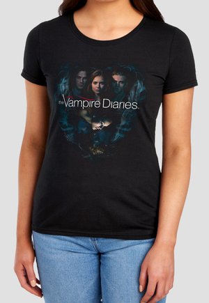 Black t-shirt with "The Vampire Diaries" text and faces of five characters in dark, smoky background worn by a person in light blue jeans.