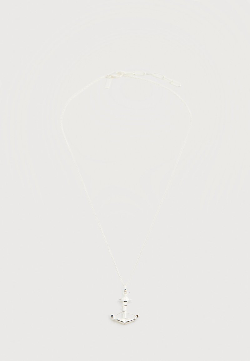 Λεπτό ασημένιο κολιέ με αλυσίδα και μικρό μενταγιόν σε σχήμα άγκυρας, σε απλό φωτεινό φόντο.