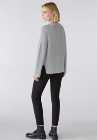 Pull gris à côtes avec une coupe décontractée, fentes latérales, associé à un pantalon noir slim et des chaussures à plateforme noires, vu de l'arrière.