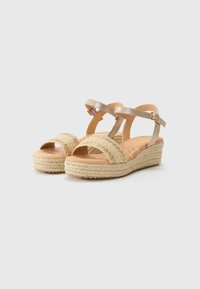 Sandales compensées avec une semelle en jute naturel, des brides texturées beiges et une bride de cheville dorée métallique. Design à bout ouvert avec une semelle plate.