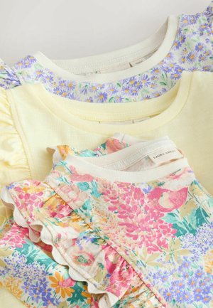 Pile di tre magliette per bambini con maniche arricciate in giallo pastello, motivo floreale viola e motivo floreale multicolore, con dettagli sullo scollo e sulle maniche.