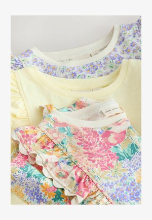 Stos trzech bluzek dziecięcych z falbankami na rękawach w pastelowym żółtym kolorze, fioletowym kwiatowym oraz wielokolorowym wzorze kwiatowym, ukazujących dekolty i detale rękawów.