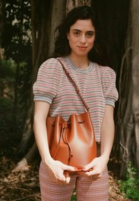 Borsa a secchiello in pelle marrone con apertura arricciata, caratterizzata da una texture liscia e un design minimalista, tenuta in mano su uno sfondo naturale.