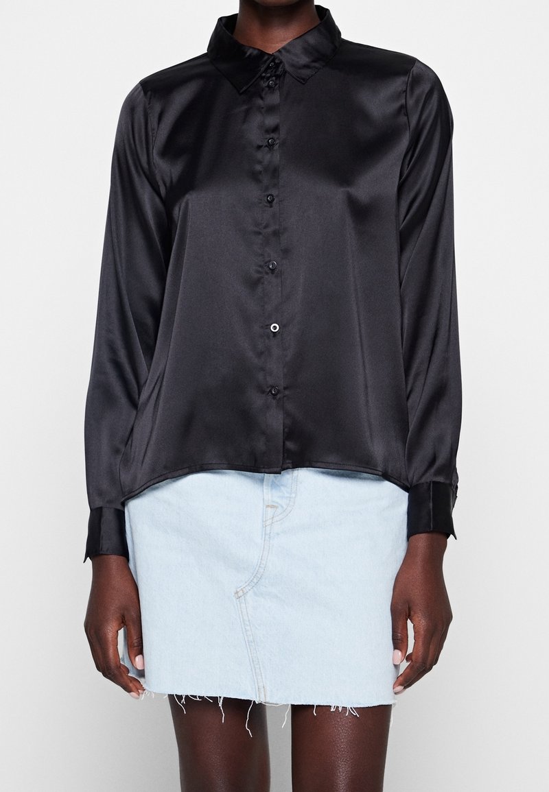 Camicia nera in satin con bottoni, colletto, maniche lunghe e orlo curvo. Abbinata a una mini gonna in denim azzurro.
