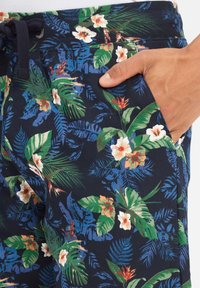 Pantaloni corti blu navy con un motivo floreale che presenta foglie verdi e fiori bianchi, realizzati in un tessuto morbido e progettati con una vita regolabile con cordino.