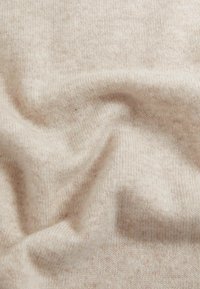 Beżowa, miękka, dziana tkanina o subtelnej teksturze i niewielkiej różnicy w odcieniu, złożona i drapowana, tworząca gładkie krzywe i fale.