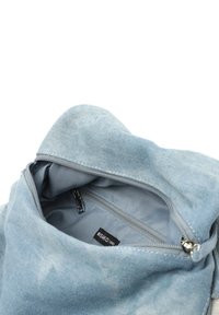 Denimväska med en mjuk, ljusblå textur. Har en dragkedjeförsedd topp och innerficka, vilket visar en enkel, funktionell design.