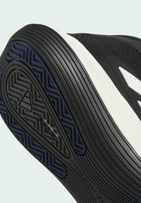 Zwarte basketbalschoen zool met een gestructureerd rubberen oppervlak, witte accenten en geometrische patronen. Bevat logo en merkinformatie.