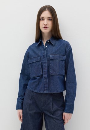 Camisa de mezclilla en azul oscuro, con dos bolsillos en el pecho, cierre de botones y mangas largas, con un diseño corto y cuello recto.