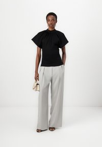Black short-sleeve top with round neckline, paired with light gray wide-leg trousers. The model holds a small beige handbag and wears black sandals.