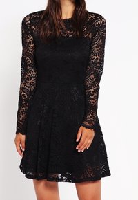 Vestido negro de encaje con mangas largas, un cuerpo ajustado y una falda acampanada. Presenta intrincados patrones florales y un escote redondo.