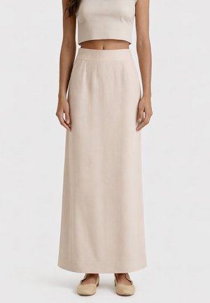 Gonna beige a vita alta, lunghezza alla caviglia, indossata con un top corto abbinato e scarpe basse beige su sfondo semplice.