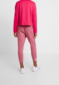 Różowy skrócony sweter z ribbowymi mankietami, w połączeniu z różowymi dresami o tapered nogawce i trzema białymi paskami na kostce. Białe sneakersy.