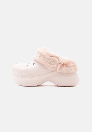 Sabots roses doublés de fourrure avec des trous de ventilation, une semelle surélevée et un bout arrondi. Texture lisse avec une bride et un bouton en guise d'accent.