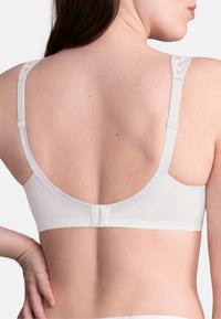 White bra featuring a smooth fabric, adjustable straps, and a hook-and-eye closure at the back. Floral accents on the straps are visible.